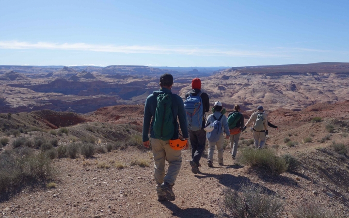 Five students hike along a trail set high above a desert landscape